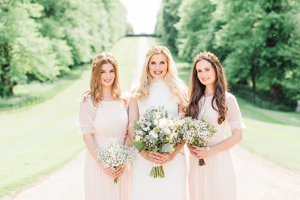 A bride and her bridesmaids hold beautiful hand-picked wedding bouquets as they stand on the grand driveway at Braxted Park wedding venue