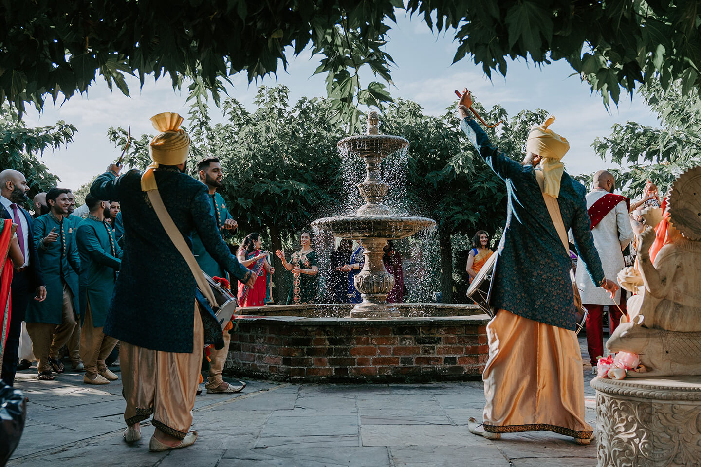 An Asian wedding band dance around the fountain in the gardens at Braxted Park luxury wedding venue in Essex